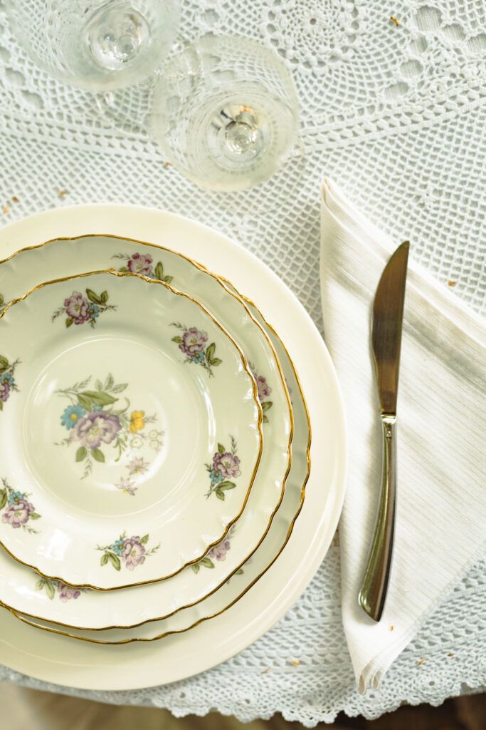 piatto vintage decorato con fiori viola su tavolo con centrino bianco, due calici e un coltello