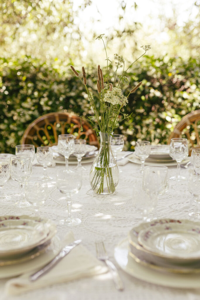 tavola apparecchiata all'aperto con piatti vintage, vaso di vetro e fiori in mezzo alla tavola