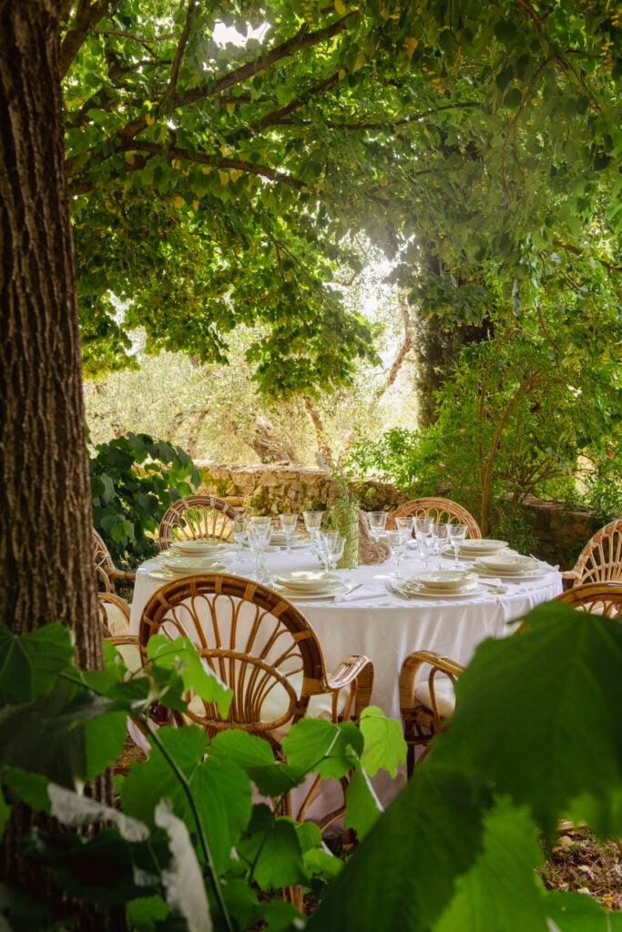 tavolo apparecchiato con tovaglia bianca e sedie in legno in un bosco