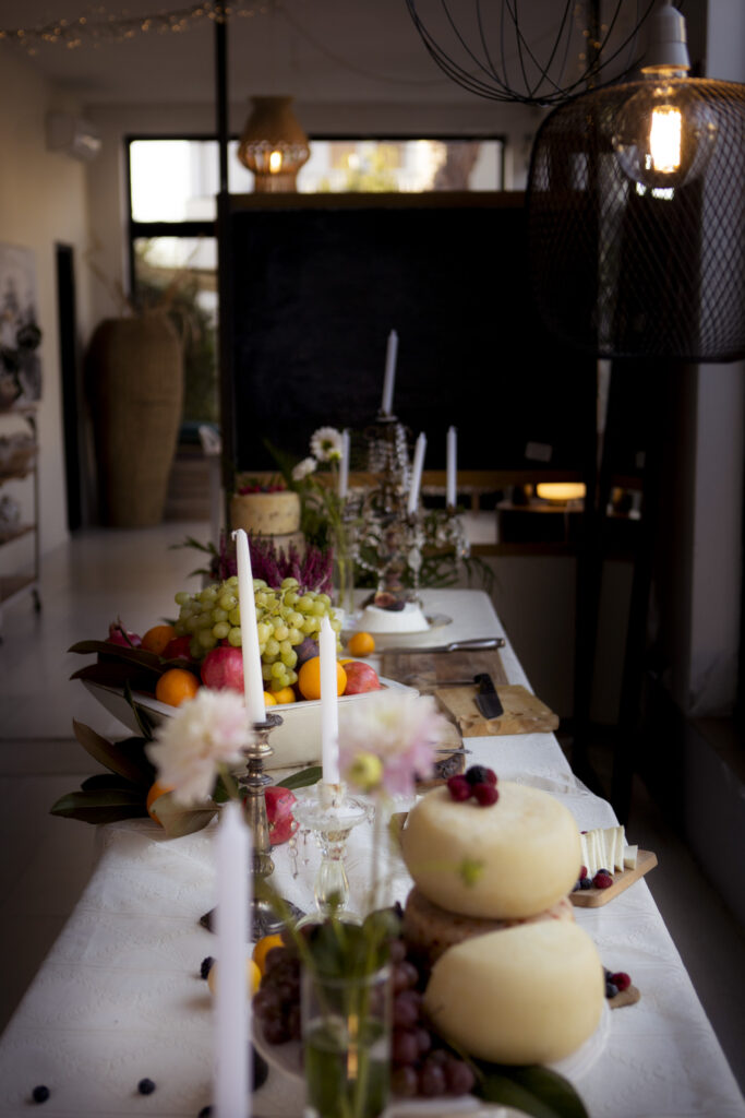 tavolo lungo all'interno con frutta in un contenitore, forme di formaggio e decorazioni di candele e fiori